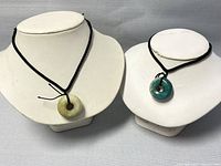 Overview of both jade donut pendants displayed on white necklace busts showing their colors and cords.
