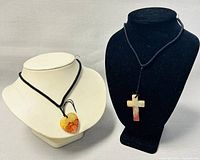 Two jade pendants displayed on black and white bust forms. One is a cross shape and the other a heart shape, both hanging on black cords.