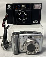 Front and side view of Minolta AF-Sv camera (black) alongside Canon PowerShot A720 IS digital camera (silver)