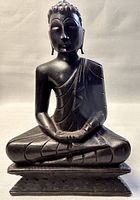 Front view of dark wooden Buddha statue seated cross-legged on base