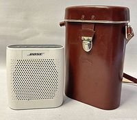Photo showing Bose Bluetooth speaker and brown leatherette carrying case for binoculars side by side on neutral background.
