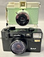 Front view showing both Minolta Hi-Matic AF and Lomography Diana Dreamer cameras stacked.