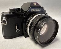 Black Nikon EM camera angled left showing Nikon branding and attached 50mm f/1.8 lens.