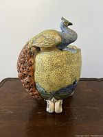 Side view of the pottery vase featuring the full peacock decoration with tail extending down side.