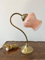 Side view of coral pink lamp with glass shade, brass-tone curved arm and base, showing cord and plug.