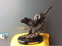 Side view of bronze-colored retriever dog statue mid-run on polished black marble base with plaque.