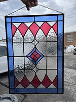 Front view of stained glass panel held by chain showing red and blue harlequin pattern over clear textured glass.