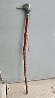 Full view of the walking cane showing the carved duck head handle and natural wood shaft against a plain background.