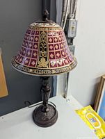 Table desk lamp with a purple and gold raised art glass bell-shaped shade atop a dark carved metal base.