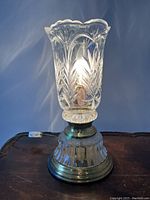 Lamp on a wooden surface, showing the crystal tulip-form etched shade and metallic base with switch and cord.