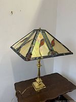 Front and side view of the lamp against wall showing brass base and stained glass shade with orange leaves and red glass jewel accents.