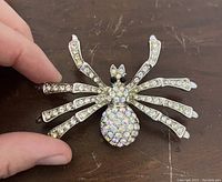 Front view of the spider brooch pin with clear and iridescent rhinestones on the body and legs held in hand, showing size and detail