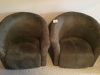 Two matching dark green upholstered round arm chairs photographed side by side against a plain wall.