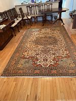Full view of the rectangular medallion design handmade Turkish rug placed on hardwood floor with traditional wooden dining chairs in the background.