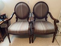 Front view of two matching arm chairs with dark wood frames and striped upholstery on seats and rounded backs