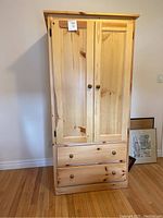 Front view of pine wood armoire showing two doors and two drawers with wooden knobs.
