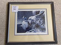Framed Stephen Lyman print of a Blue Jay on a snowy branch with a cream-colored mat and dark grey frame, photo taken from the front.