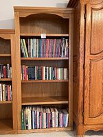 Full view of the solid wood bookcase filled with assorted books on three shelves with two empty shelves.