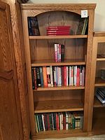 Front view of solid wood bookcase filled with books including the red Christmas books and cookbooks.