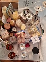 Overview of assorted candles, candle holders, decorative vase, and snuffer on a table including candles in jars, wax tealights, and various shapes.