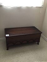 Front side view of dark wood cedar chest with scalloped carving at base and short squat feet.
