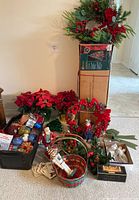 Overview of assorted Christmas decorations including wreaths, poinsettias, ornaments, nutcracker figures, a basket, and other decorative items arranged on the floor.