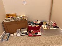 Wide view showing multiple boxes and trays containing assorted costume jewelry items arranged on carpet.