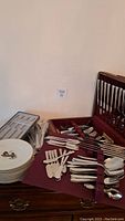 Flatware pieces spread on table next to open wooden box and stacked plates