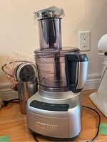 Silver Cuisinart food processor with clear plastic container and black handle, shown assembled on countertop.