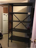 Front view of a black metal shelving unit with five shelves inside a room, showing the shelving's structure and cross-bracing on back.