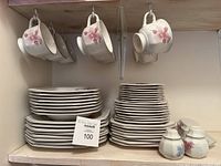 Stack of plates, bowls on shelf with hanging teacups and saucers visible, butter dish and salt and pepper shakers on the right