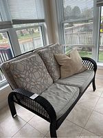 Front view of black resin loveseat with two seat cushions in light gray and two patterned back cushions, with one additional decorative beige pillow.