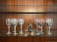 Full view of six wine glasses arranged with glass bowls and intricate pewter stems and bases shaped with grape clusters and leaf motifs.