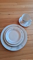 Set of place setting items including plates and cup with saucer on wooden floor