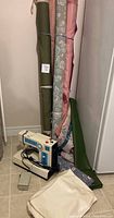 Full lot view showing sewing machine with foot pedal and assorted fabric rolls in various colors and patterns standing against a wall on a tiled floor.