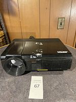 Front angle view of black Aspen projector showing lens, surface wear, and sticker residue.