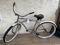 Side view of the full bicycle showing silver frame with white fenders and whitewall tires, large black seat, upright handlebars, and kickstand.