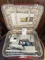 Brother sewing machine packed in an ornate vintage carrying case, showing machine, cords, and pedal.
