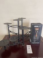 Black metal multi-tier candle holder with circular platforms displayed on wood surface alongside the boxed Gillette Labs heated razor set.