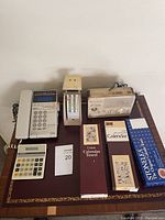 Wide shot showing all items on a wooden surface including calculators, phone, clock radio, and calendars