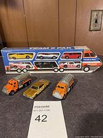 Overall view of Hot Wheels Team 6 Pak boxed set of six die-cast cars with three additional die-cast vehicles (two construction trucks and one gold car) placed in front.
