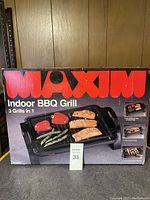 Box front showing WOXIM Indoor BBQ Grill with grilled food on the non-stick die cast plate.