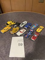 Lot of 10 vintage Matchbox and other toy cars arranged on table including taxis, race cars, and construction vehicle.