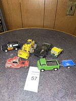 Seven toy vehicles on round table with wood panel background.