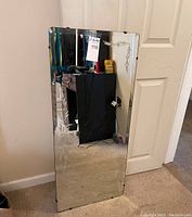 Rectangular mirror mounted on white wall showing etched floral designs and beveled edges, with corner mounting clips visible.