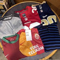 Six different jerseys and shirts laid out on a round table showing NFL football jerseys, soccer jerseys, and casual shirts