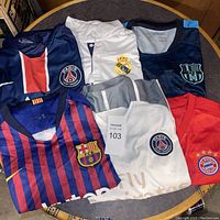 Photo showing six soccer jerseys from European clubs in various colors and sizes displayed on a circular wooden surface.