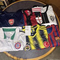 Photo shows seven different soccer jerseys with various club logos and mixed sizes.