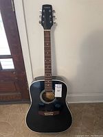 Front full-length view of the black Texarkana acoustic guitar against a white wall and floor.