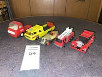Five toy vehicles shown on a table against wood panel background.